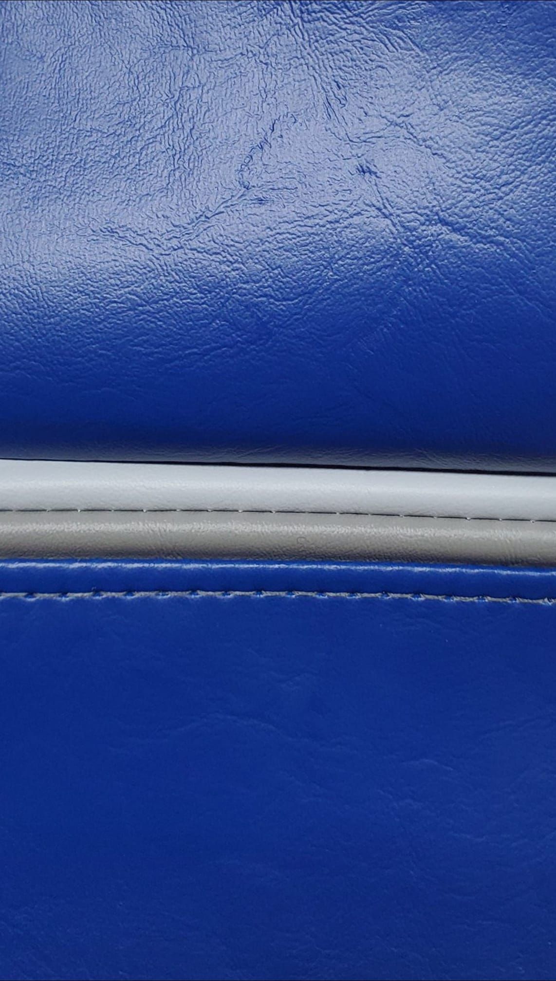 Close-up of royal blue leather with a silver strip and stitching between panels.