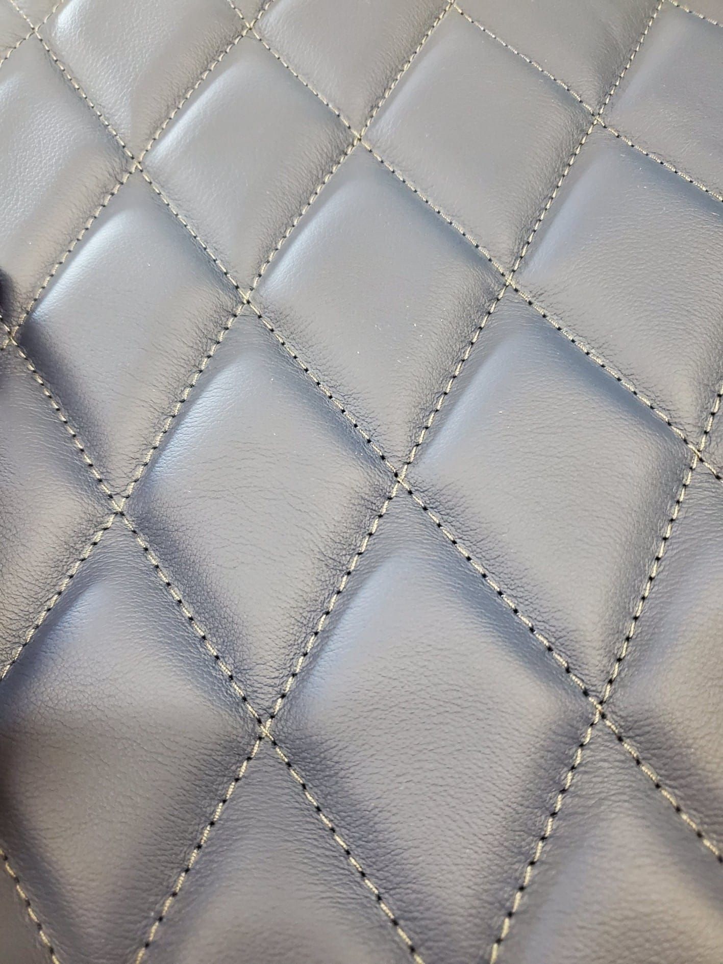 Close-up of gray leather with diamond-shaped quilted stitching.