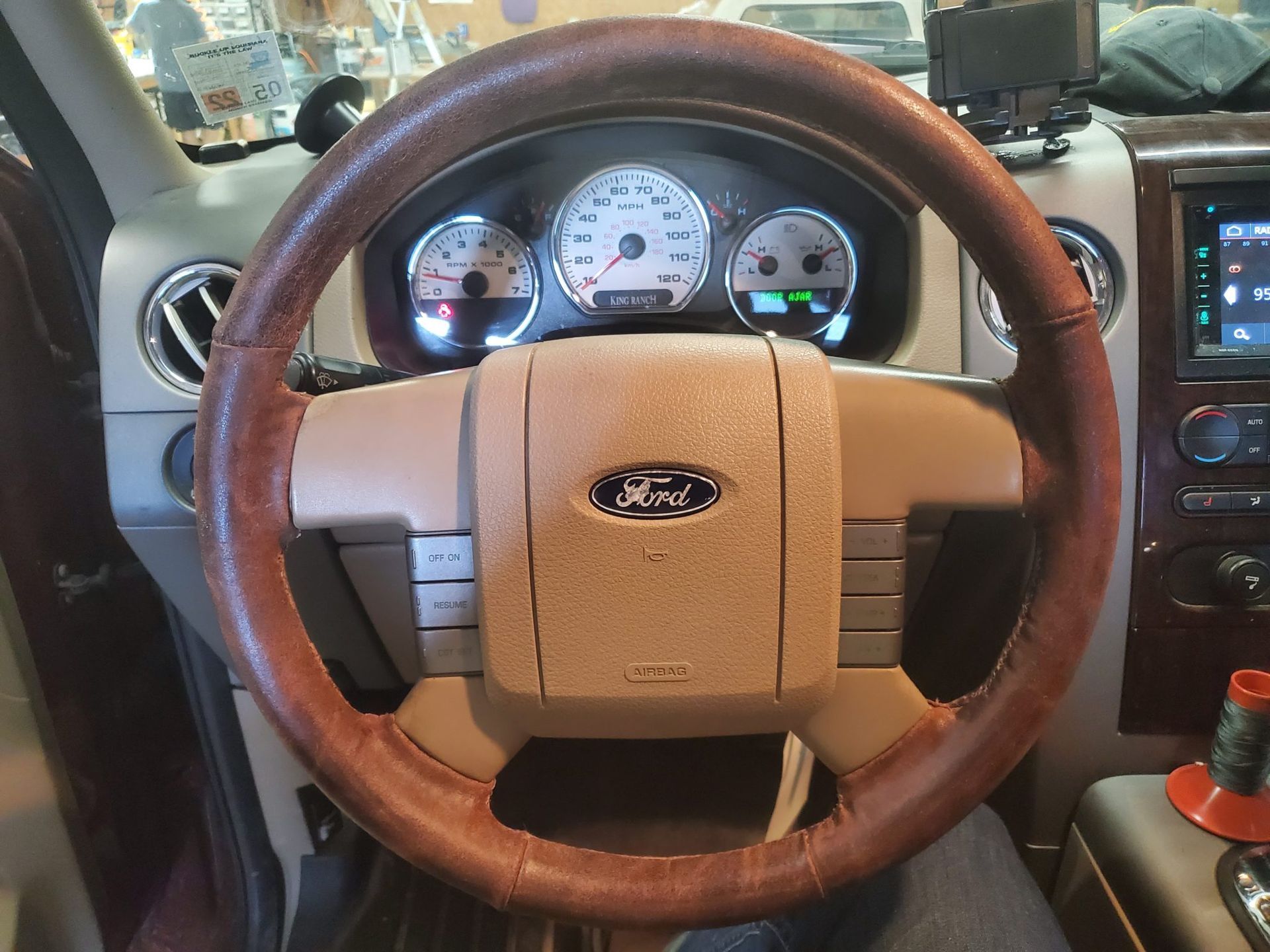 Brown leather-wrapped steering wheel in a Ford truck. Tan dashboard, gauges, and radio are visible.