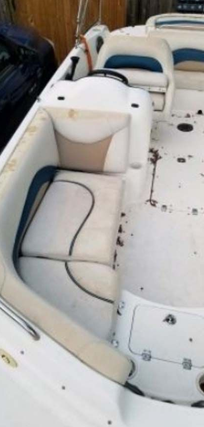 Boat interior with white and tan seats, dirty flooring. Steering wheel visible.