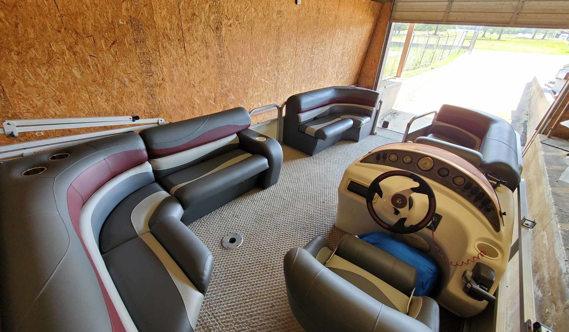 Pontoon boat interior with seating, dashboard, and view of the outside.