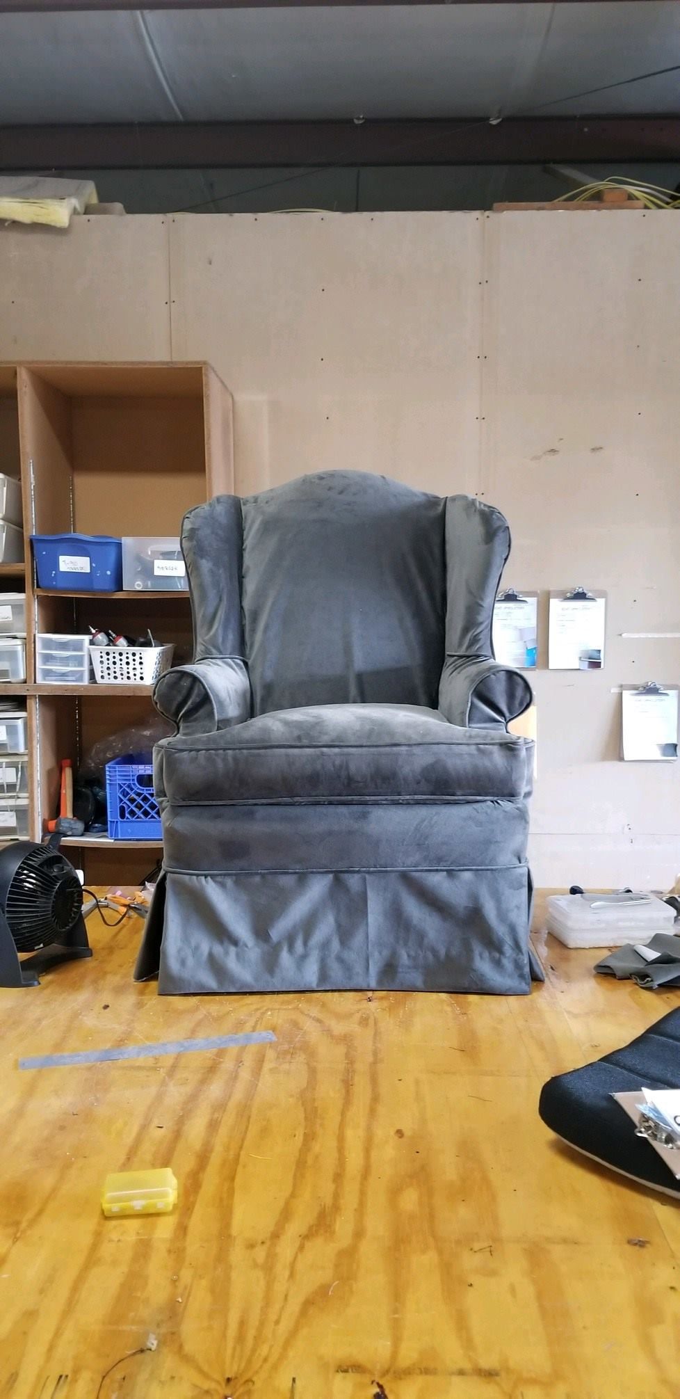 A worn, blue wingback chair sits on a wooden surface, in a workshop setting.