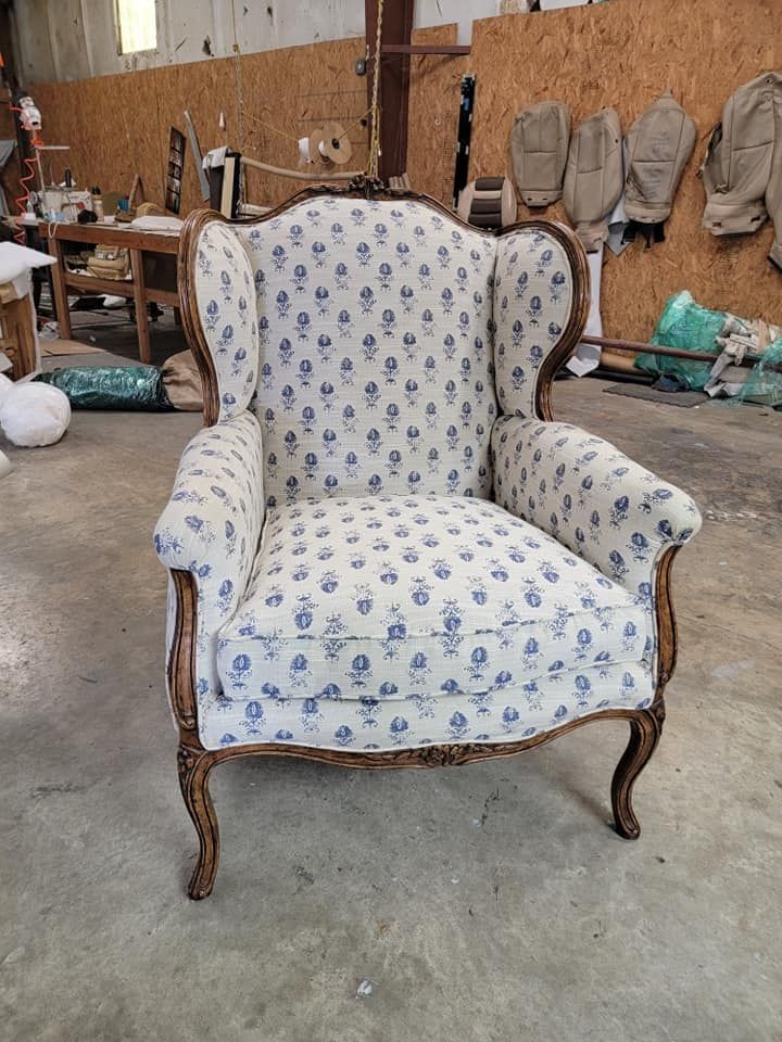 Wingback armchair with white and blue floral fabric, brown wood frame, in workshop.