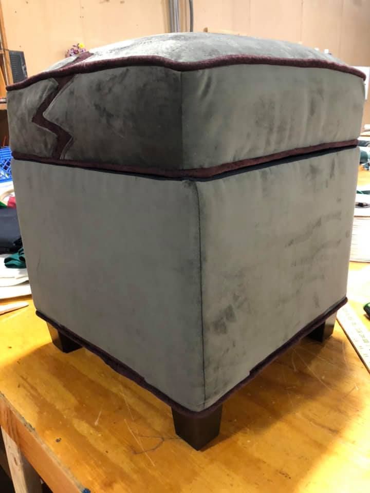Gray and maroon upholstered ottoman on a wooden table.
