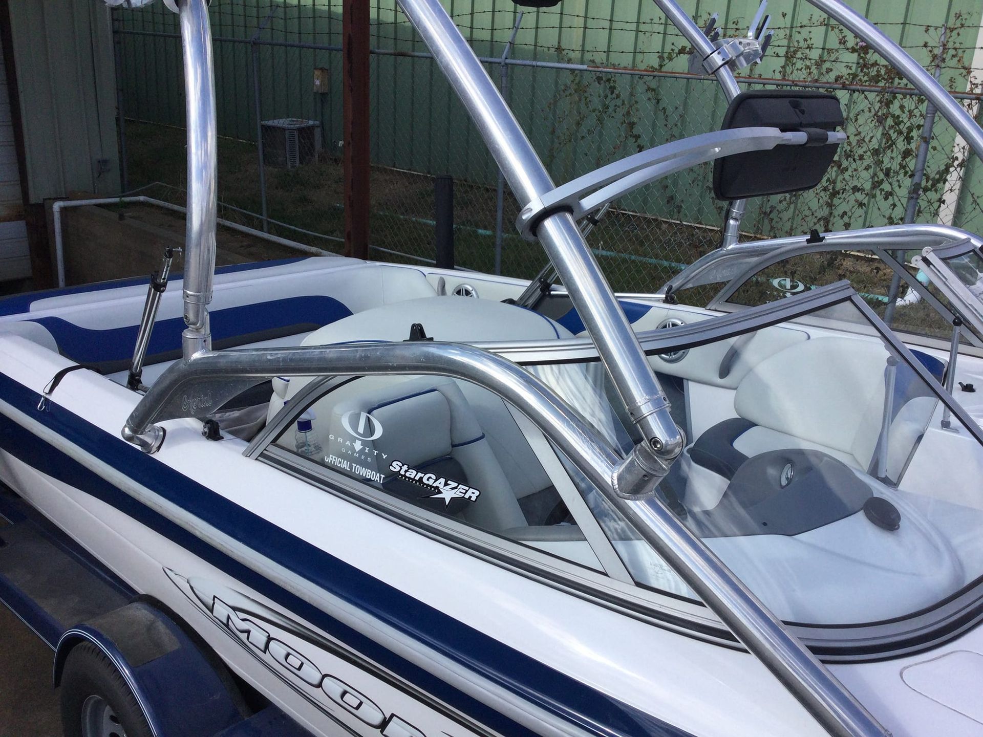 White and blue boat with metal wakeboard tower, on a trailer.