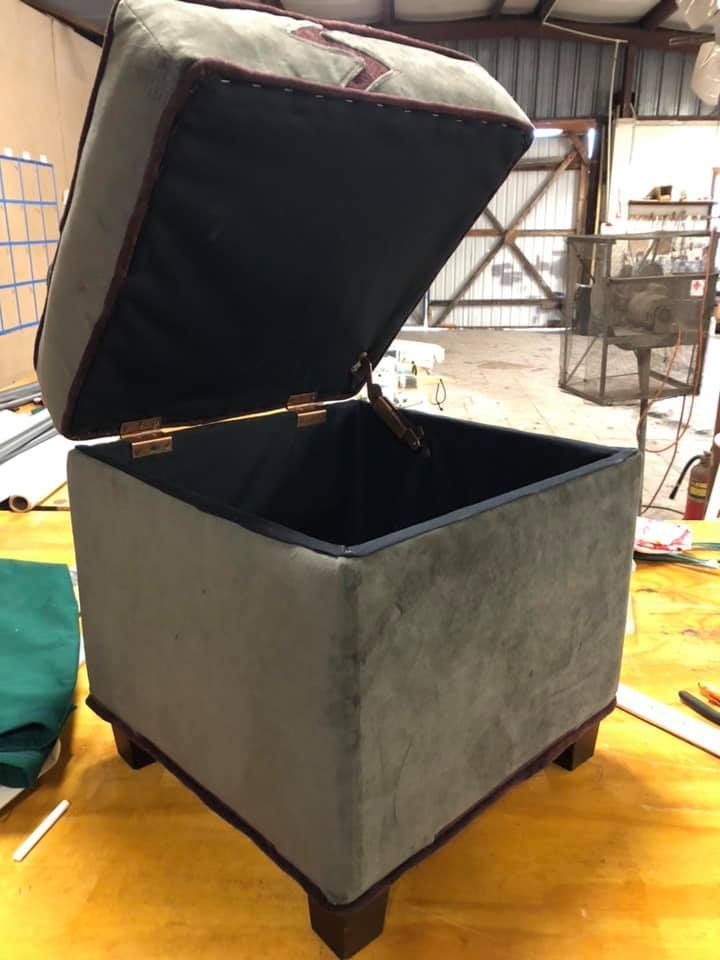 A gray velvet storage ottoman with the lid open, revealing an empty interior.