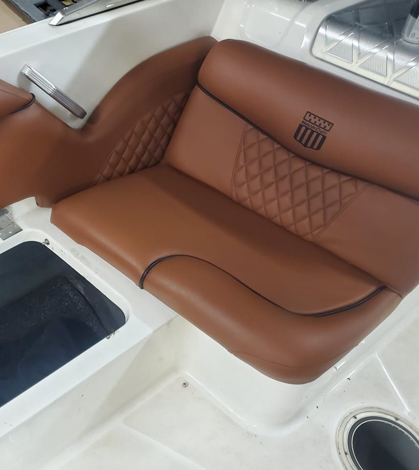 Brown leather boat seat with diamond stitching and emblem, white interior.