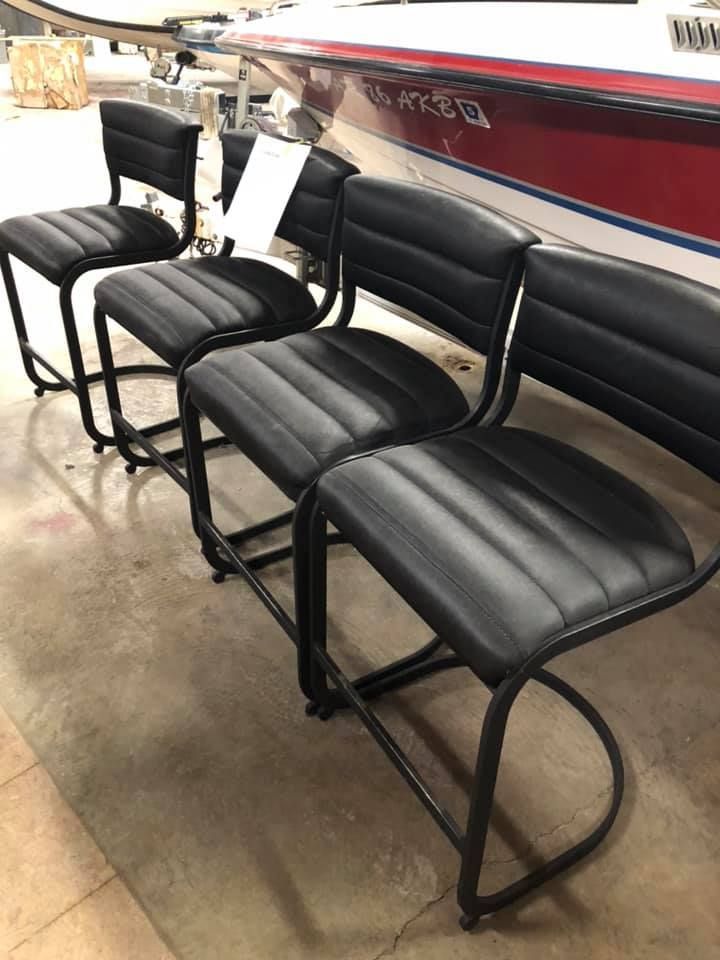 Four black leather bar stools with metal frames in a warehouse setting.