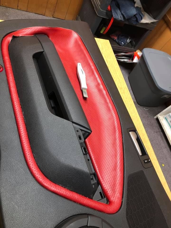 Car door panel with red leather and black trim, a utility knife resting on it.
