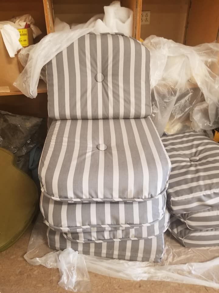 Stack of gray and white striped chair cushions with a button detail, on a wooden shelf.