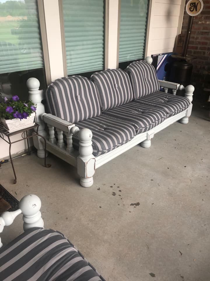 Outdoor sofa with gray and white striped cushions, on a porch with brick wall and blinds.
