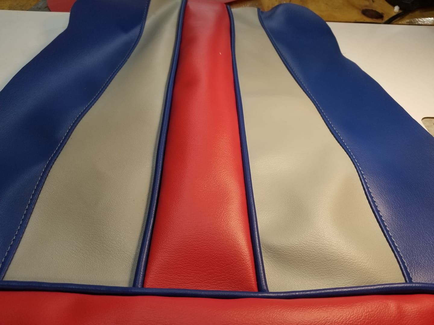 Close-up of a multi-colored vinyl upholstery piece; red, blue, and gray sections with piped edges.