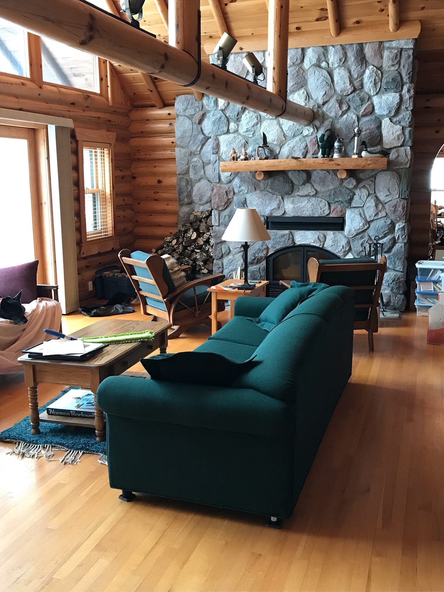 Cozy cabin living room with teal sofa, stone fireplace, and log walls.