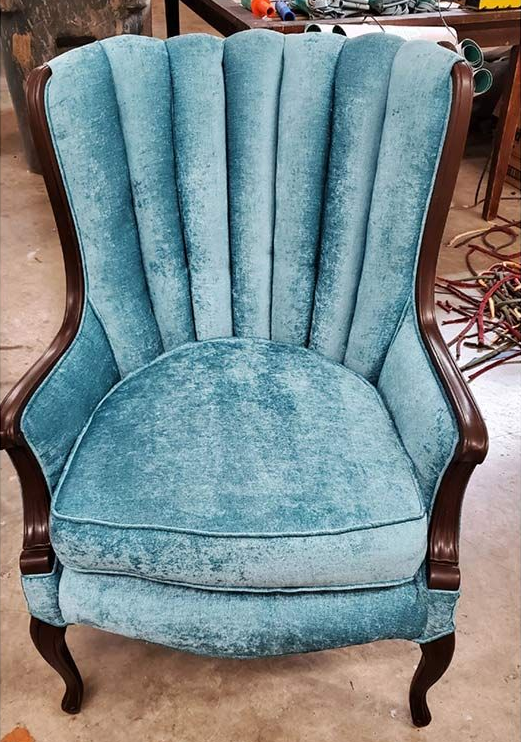 Teal velvet wingback chair with dark wood frame, set against a blurry background.