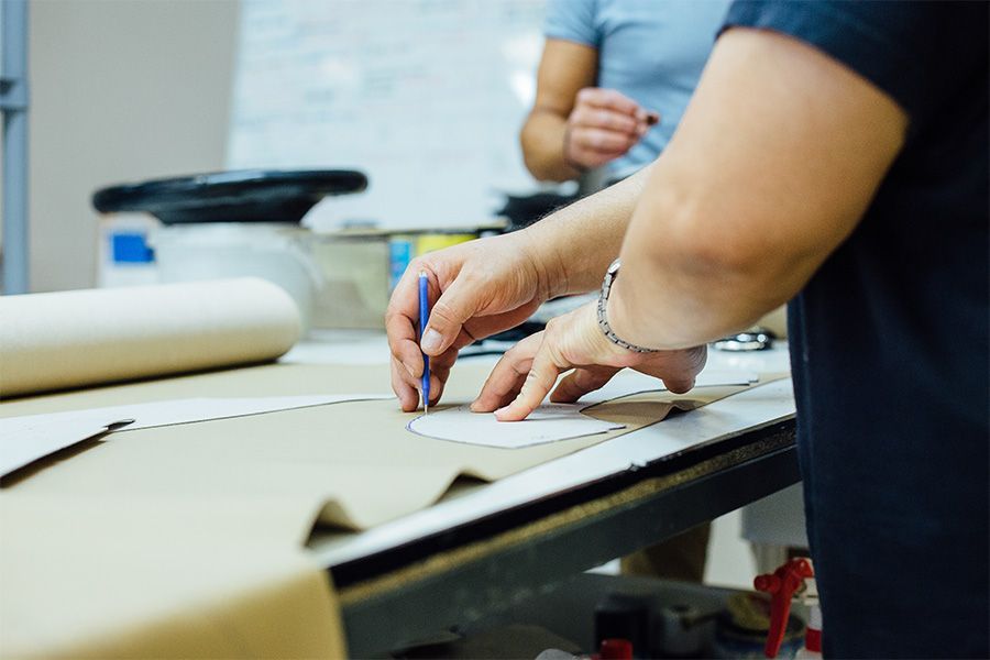 Person tracing a pattern onto fabric on a table; another person in background.