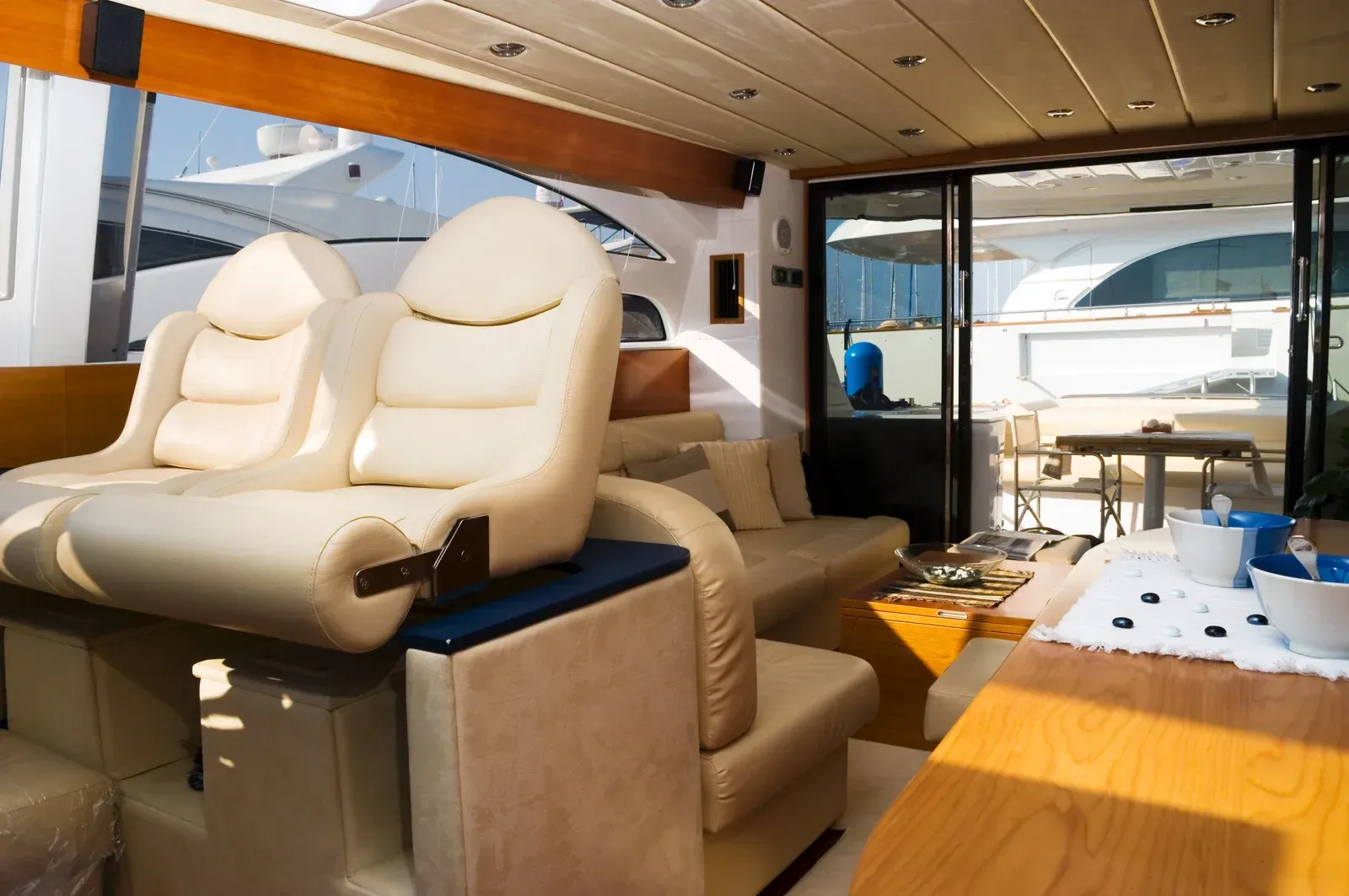 Interior of a luxury yacht, featuring cream leather seating, wooden accents, and an outdoor view.