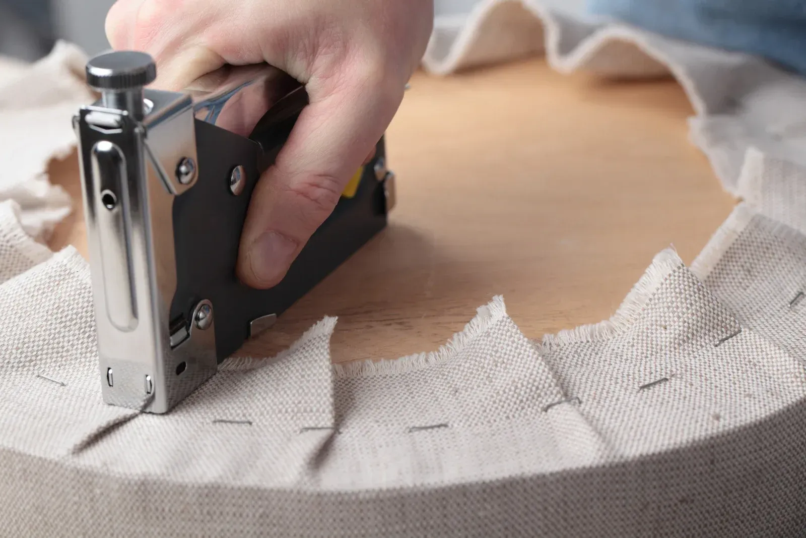 Person stapling fabric to a wooden surface, crafting or reupholstering something.