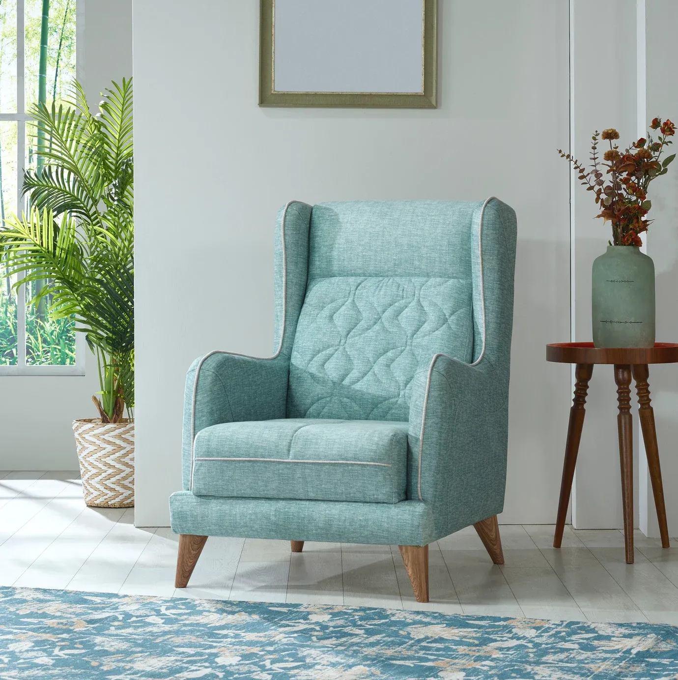 Teal armchair with high back in a living room, next to a small side table and a large plant.
