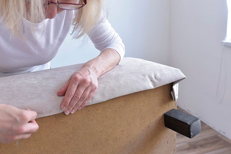 Woman reupholstering a beige sofa, holding fabric, indoors.