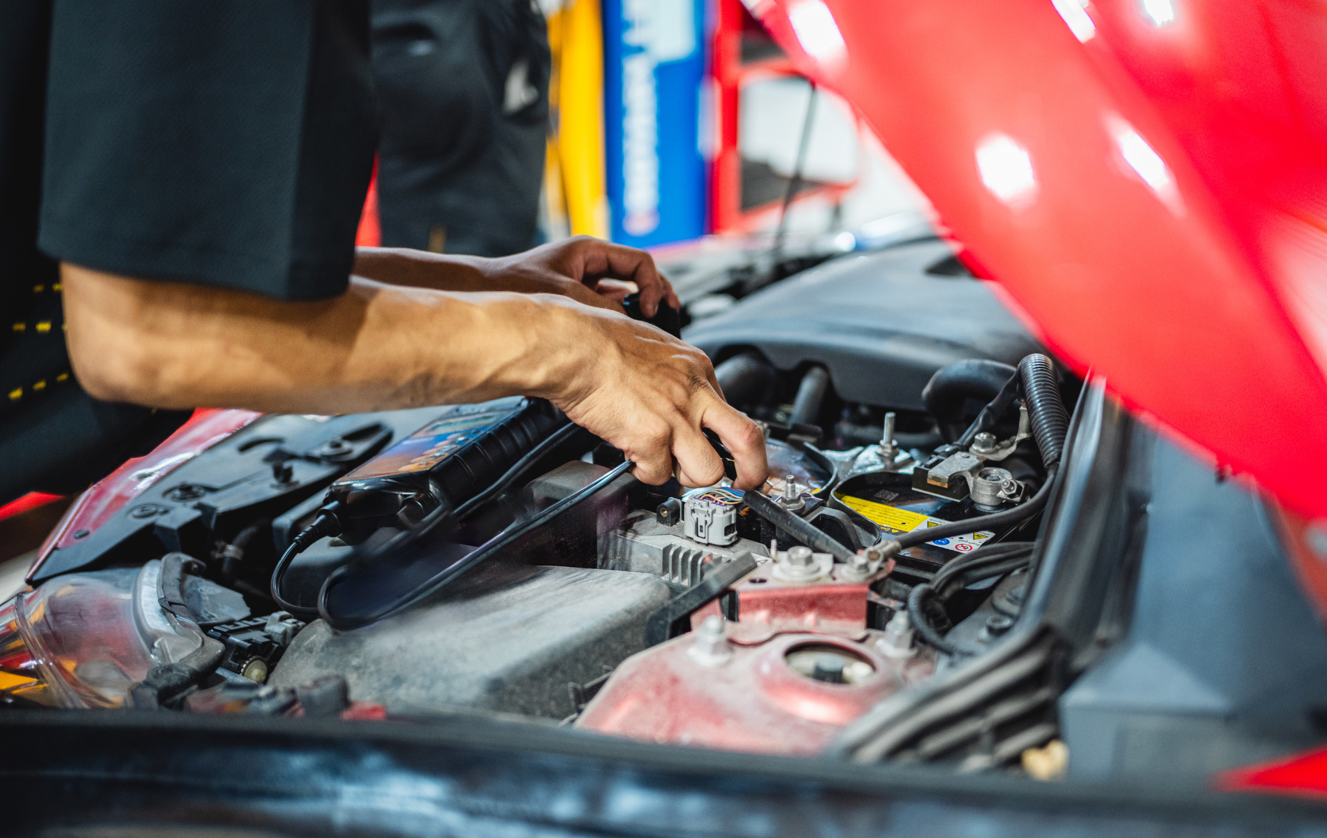 Mechanic working on a red car's engine with the hood open, in a garage.