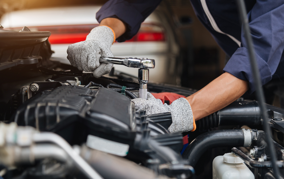 Mechanic using a wrench to repair a car engine, wearing gloves.