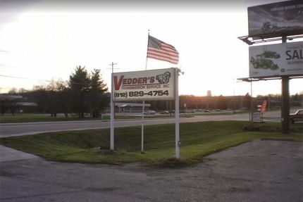 Sign for Vedder's Automotive Service with American flag on a grassy corner at dusk. A billboard is to the right.