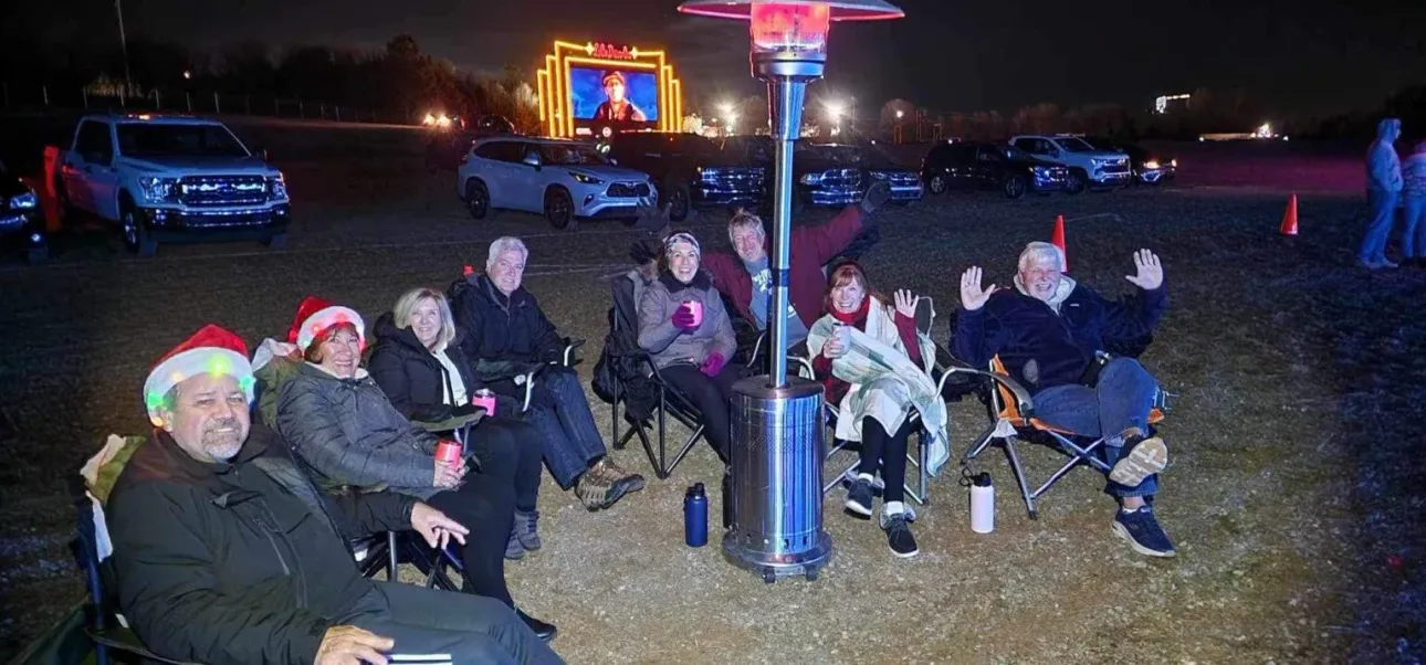A group of people are sitting around a fire pit in a parking lot at night.