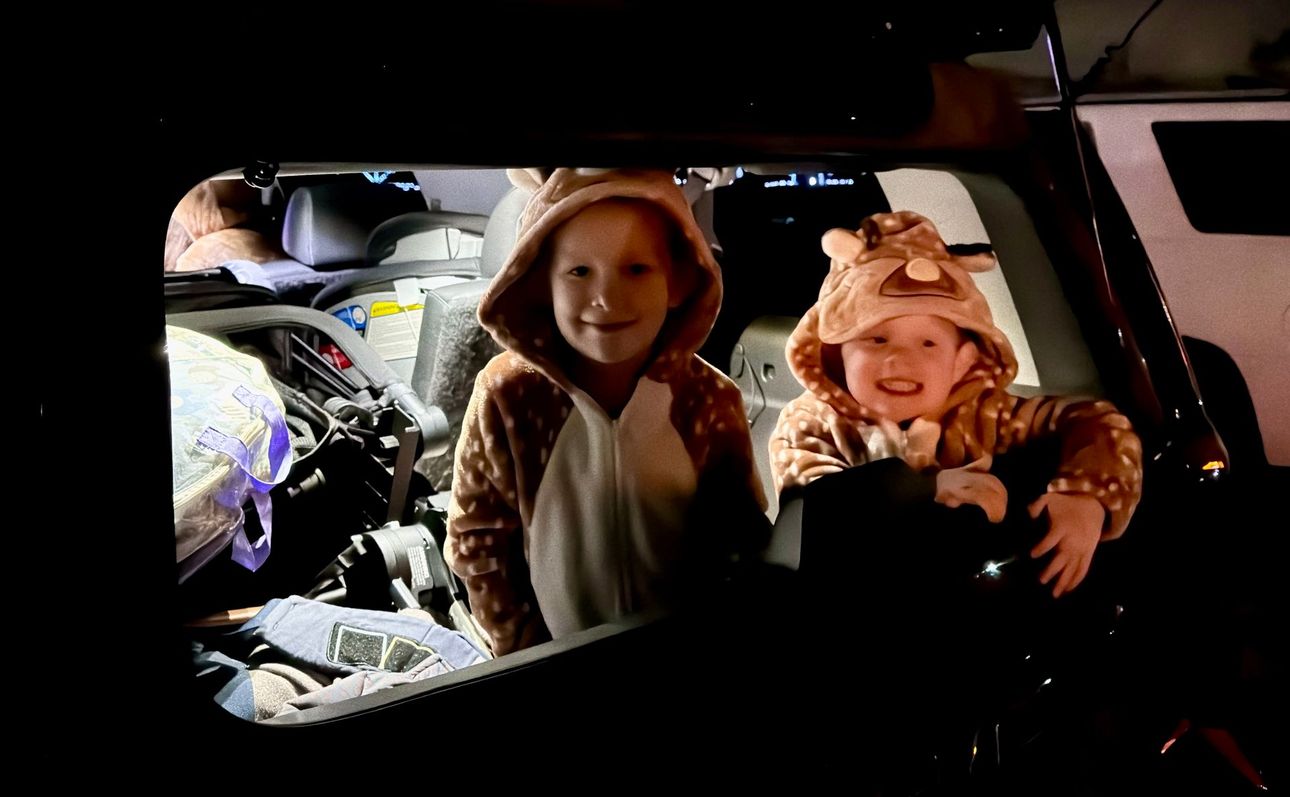 Two children in costumes are sitting in the back of a car.