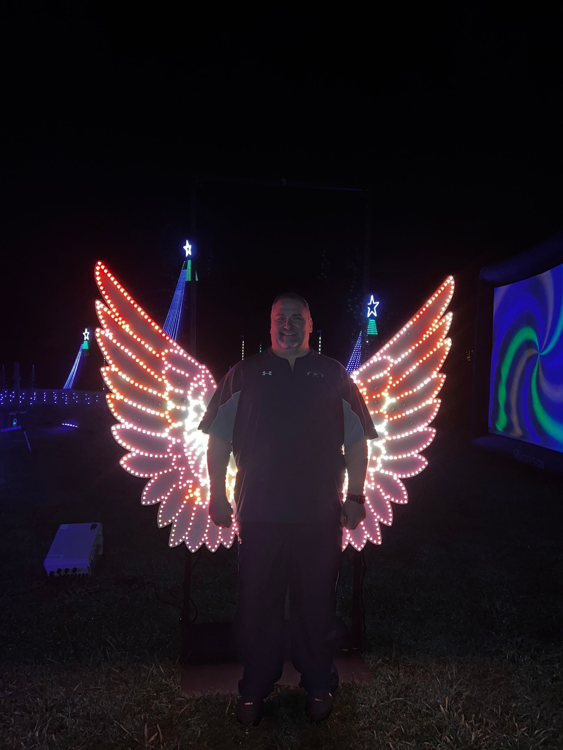 A man with wings made of lights is standing in the dark
