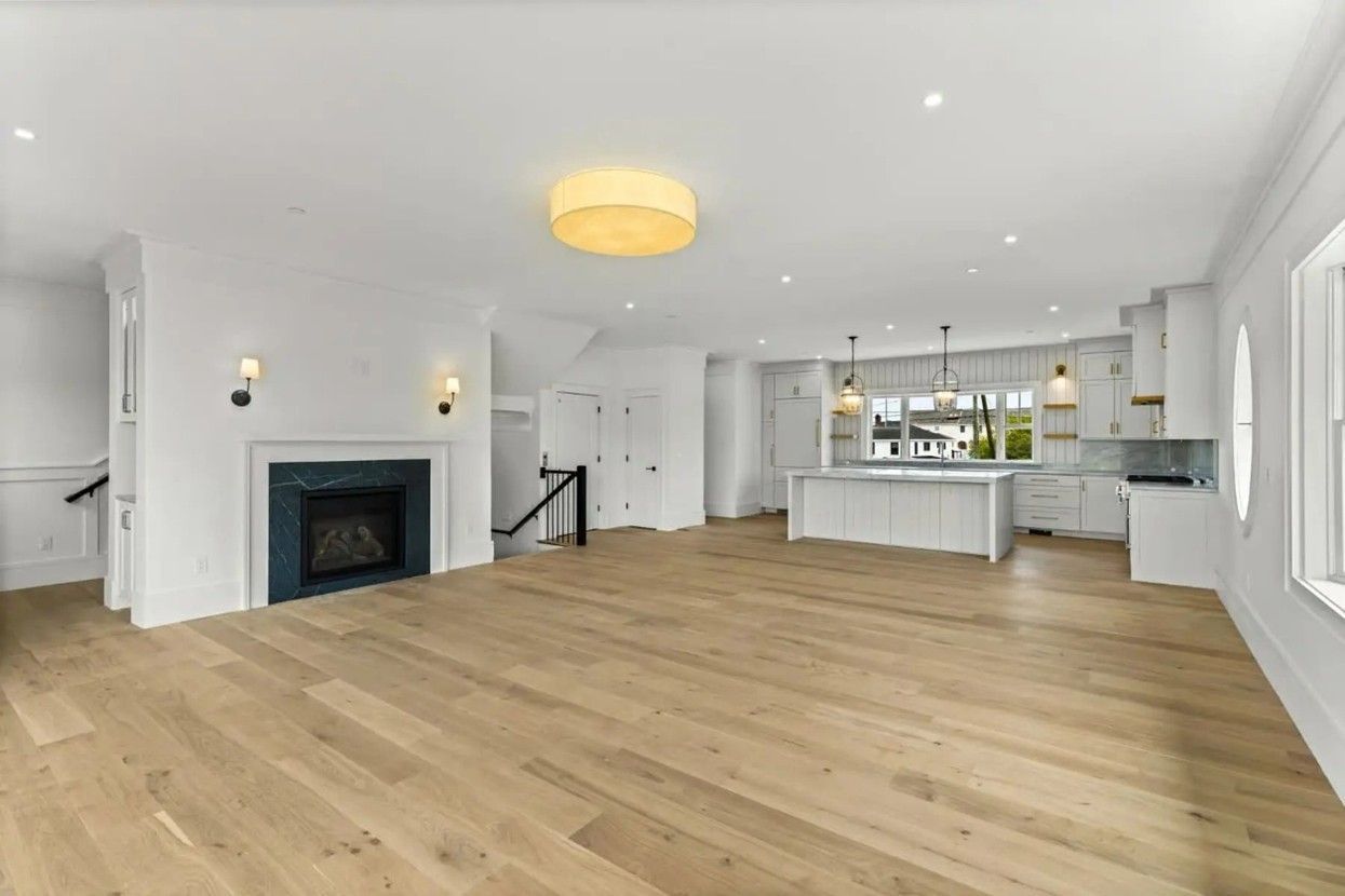 Spacious, bright living area with light wood floors, fireplace, and open kitchen.