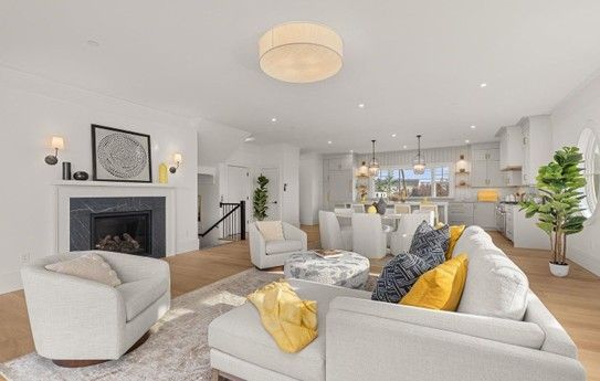 Bright, airy living room with fireplace, white furniture, and open kitchen in the background.