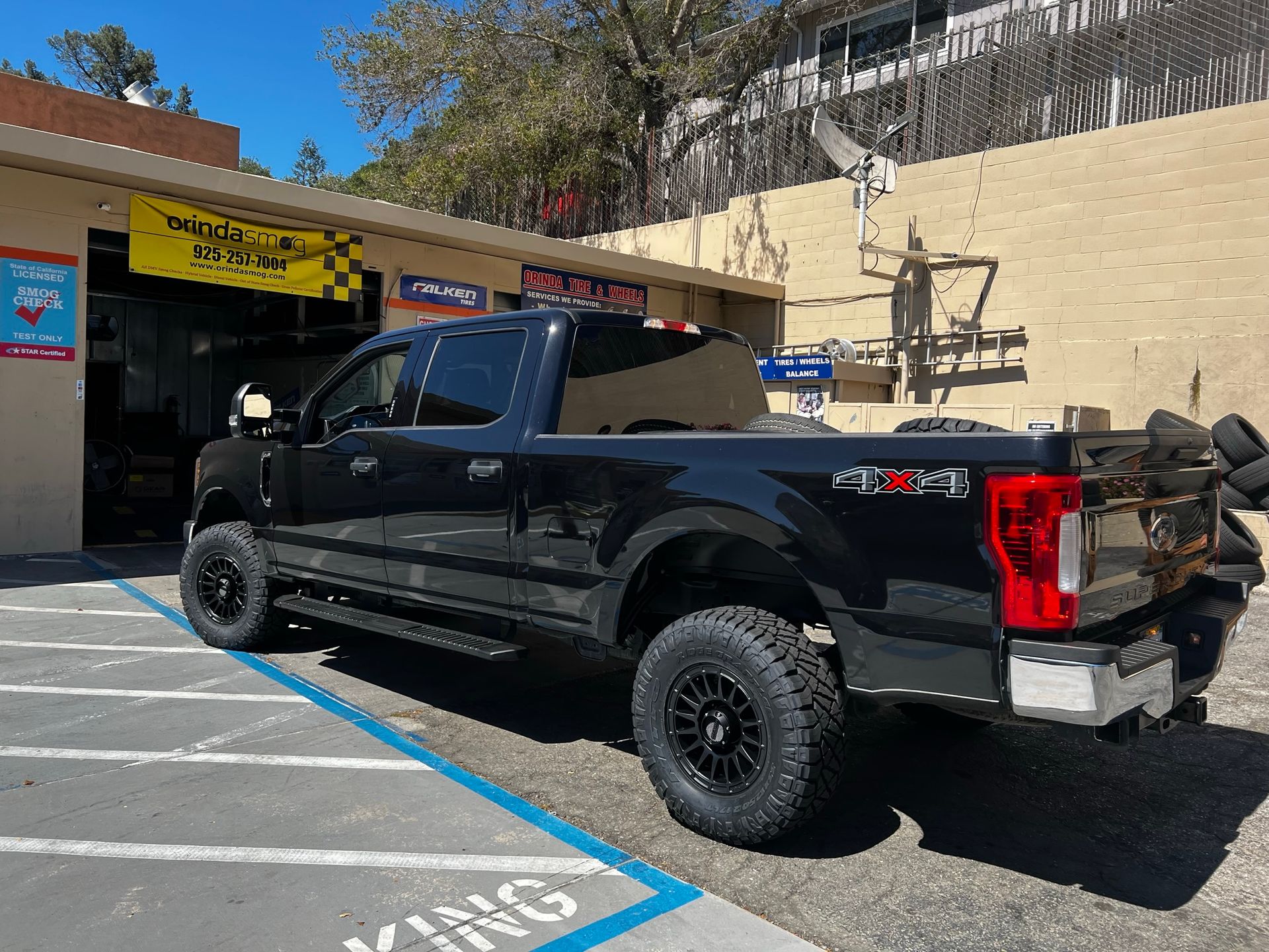 A black Ford pickup truck parked in front of an automotive shop under a bright, sunny sky.