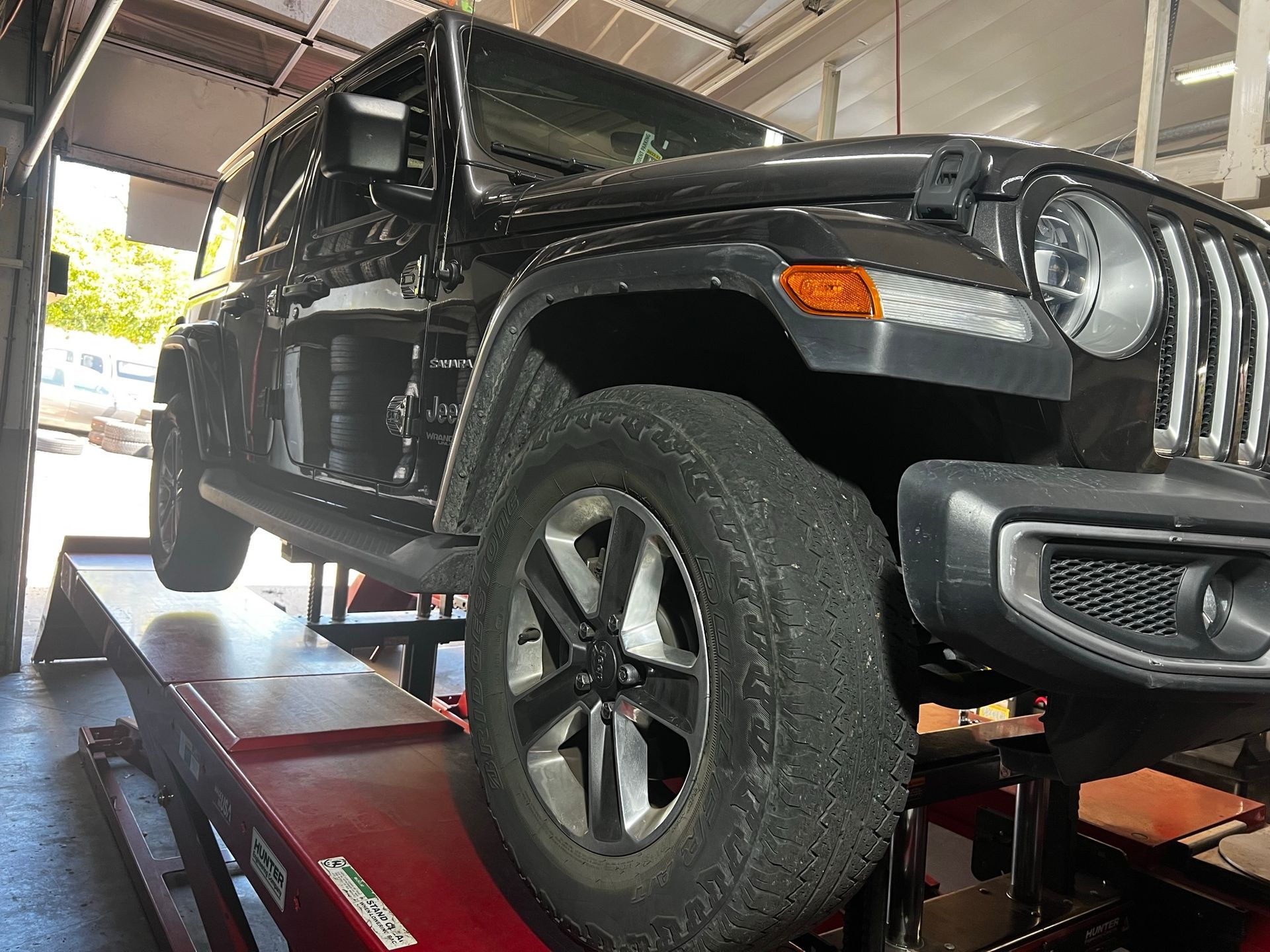 A black Jeep parked on a red hydraulic lift inside an auto repair shop.