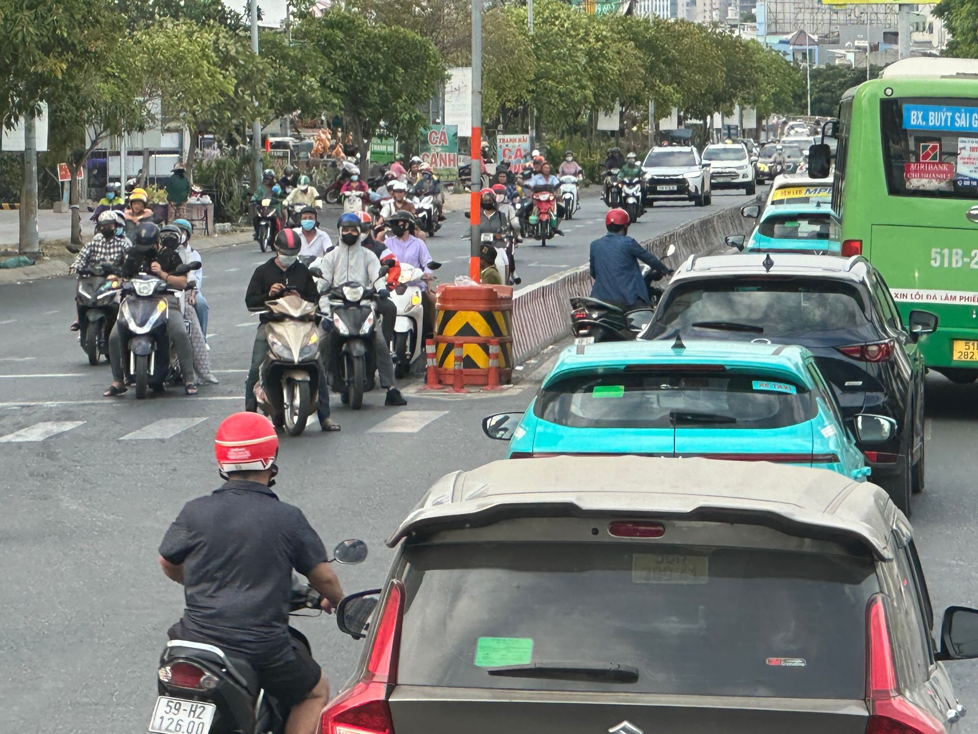 Traffic scene in a city featuring a green bus, several cars, and many motorcyclists waiting in a multi-lane intersection.