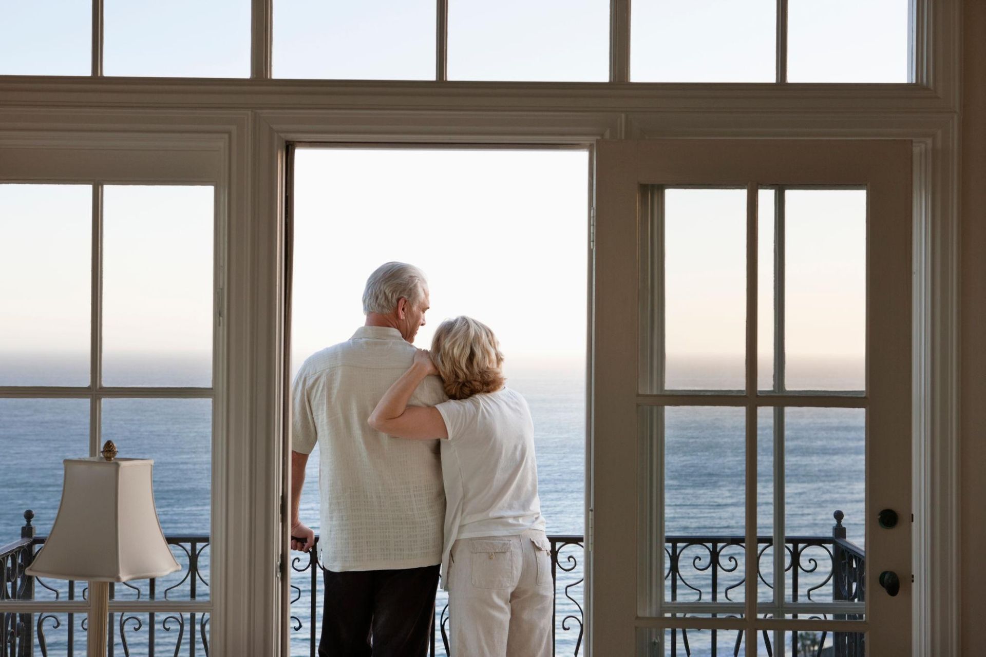 A man and woman are standing in a doorway looking out onto the ocean. The woman has her hand on the man's shoulder.