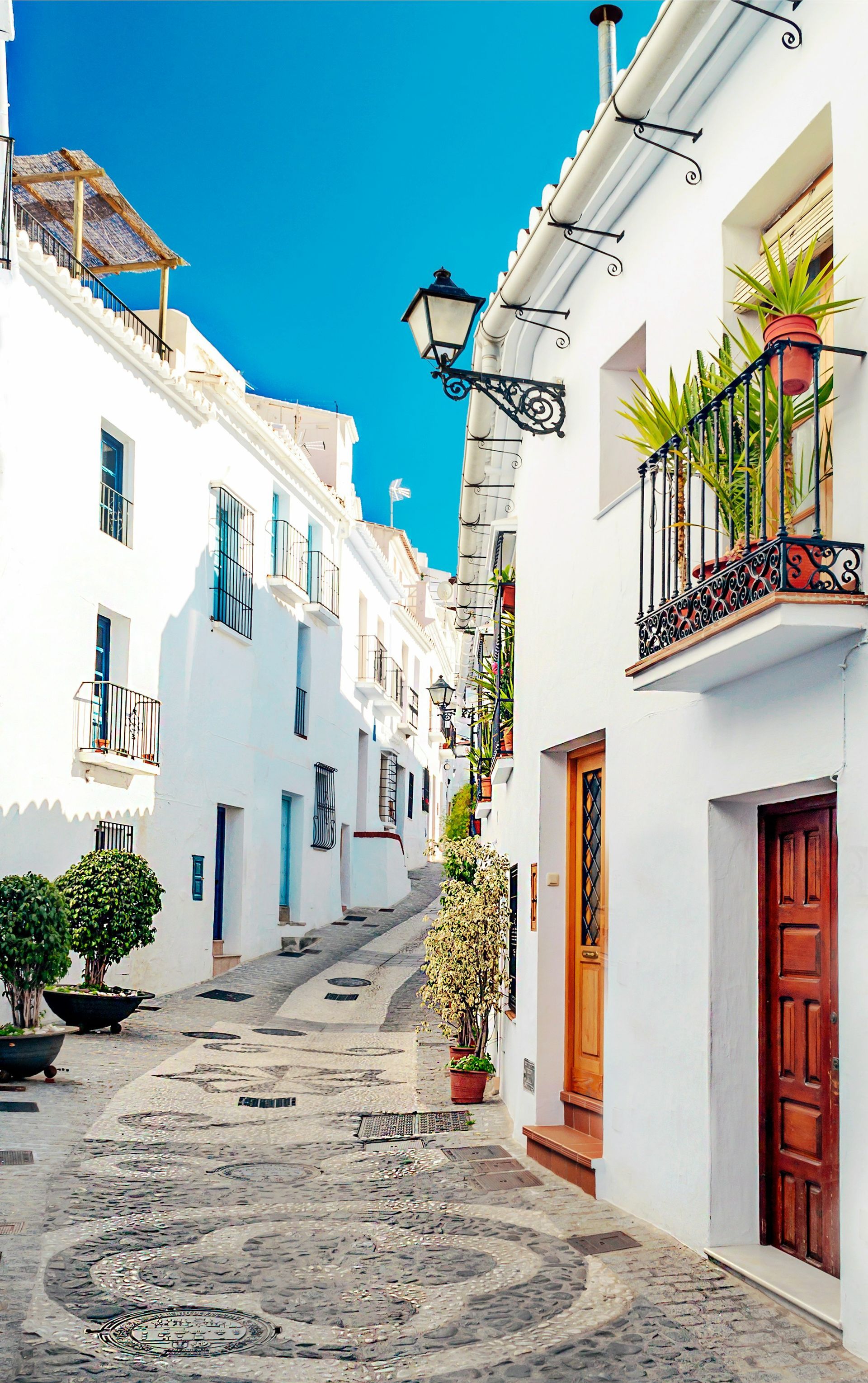Narrow whitewashed street with blue doors, cobblestone path, and a bright blue sky.