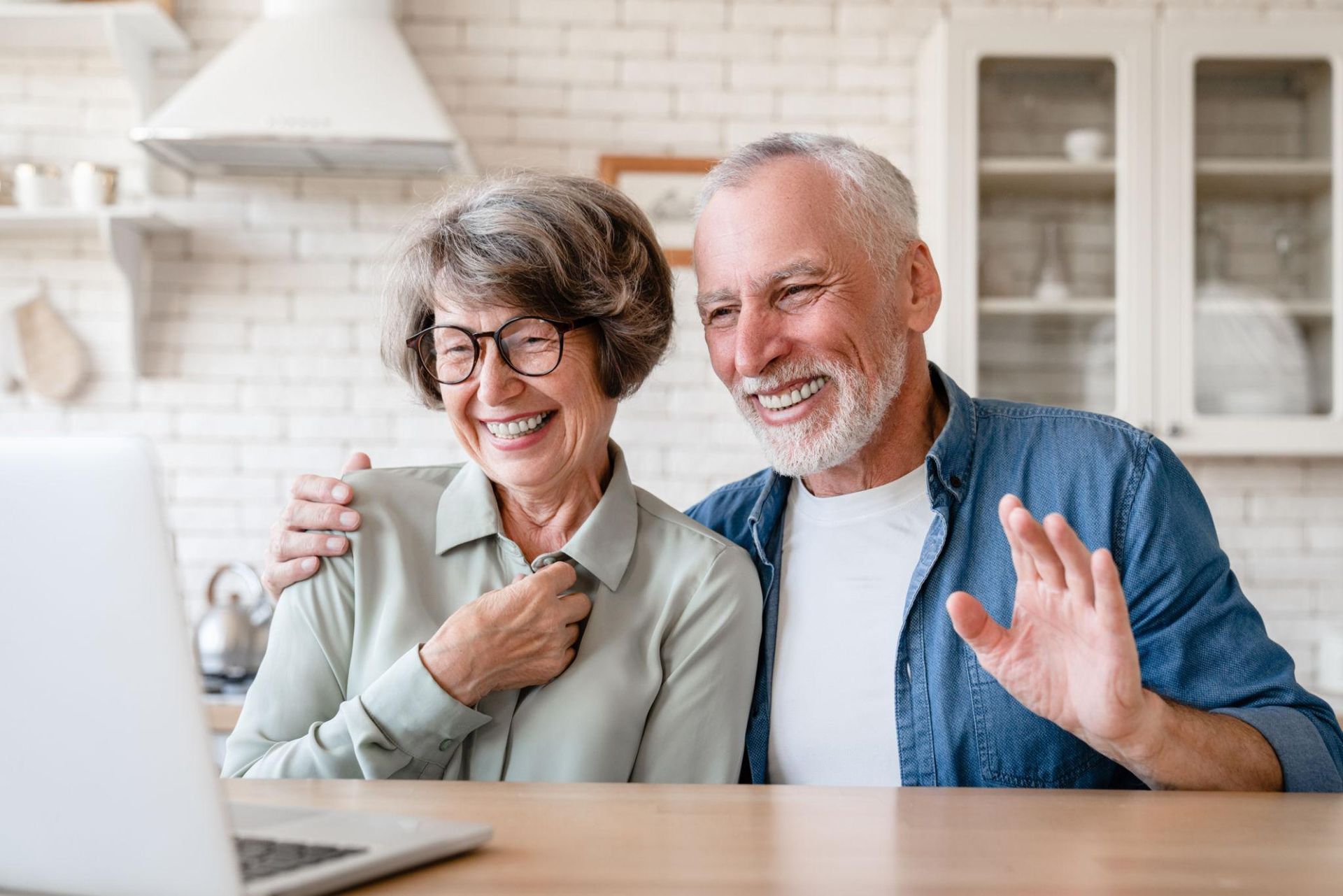 Smiling couple waving during a video call in a bright kitchen
