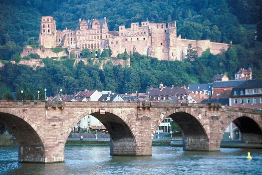 Stone bridge over a river with a fortress on a wooded hill in the background