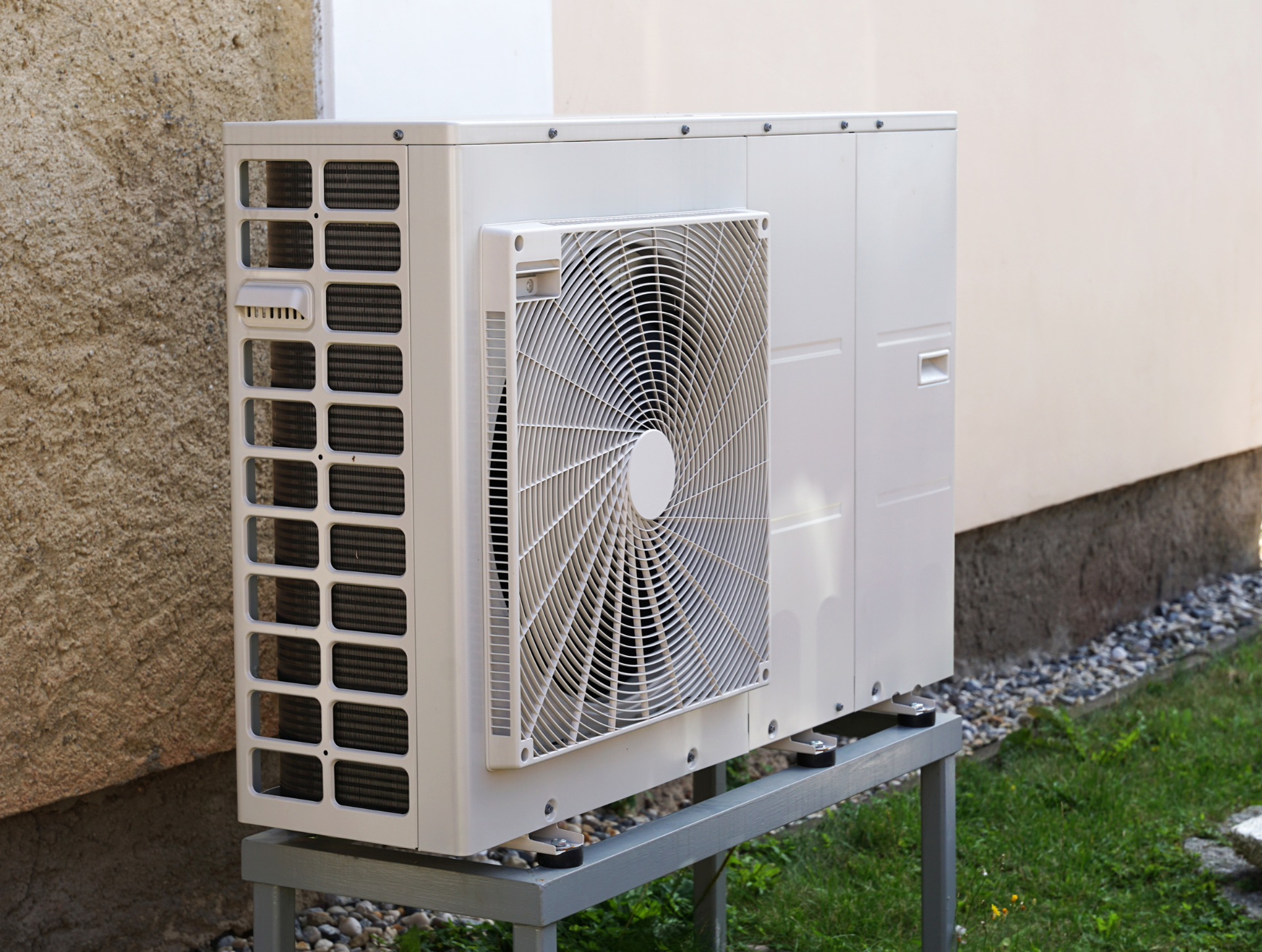 White air conditioning unit mounted outside a building on a metal stand.