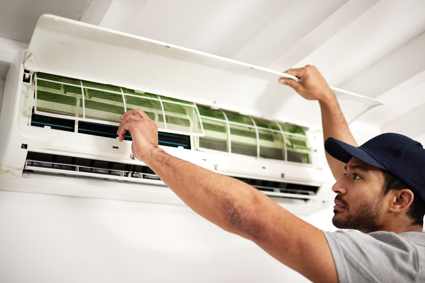A man is cleaning an air conditioner on the wall.