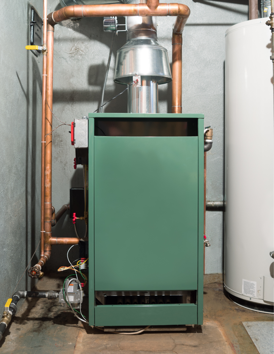 Green furnace with copper pipes in a basement setting next to a water heater.
