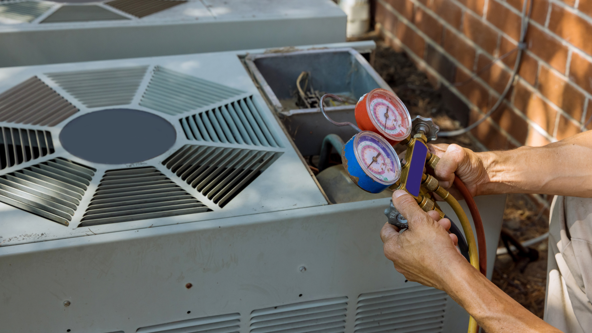 A man is working on an air conditioner outside of a brick building.