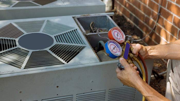 A man is working on an air conditioner outside of a brick building.