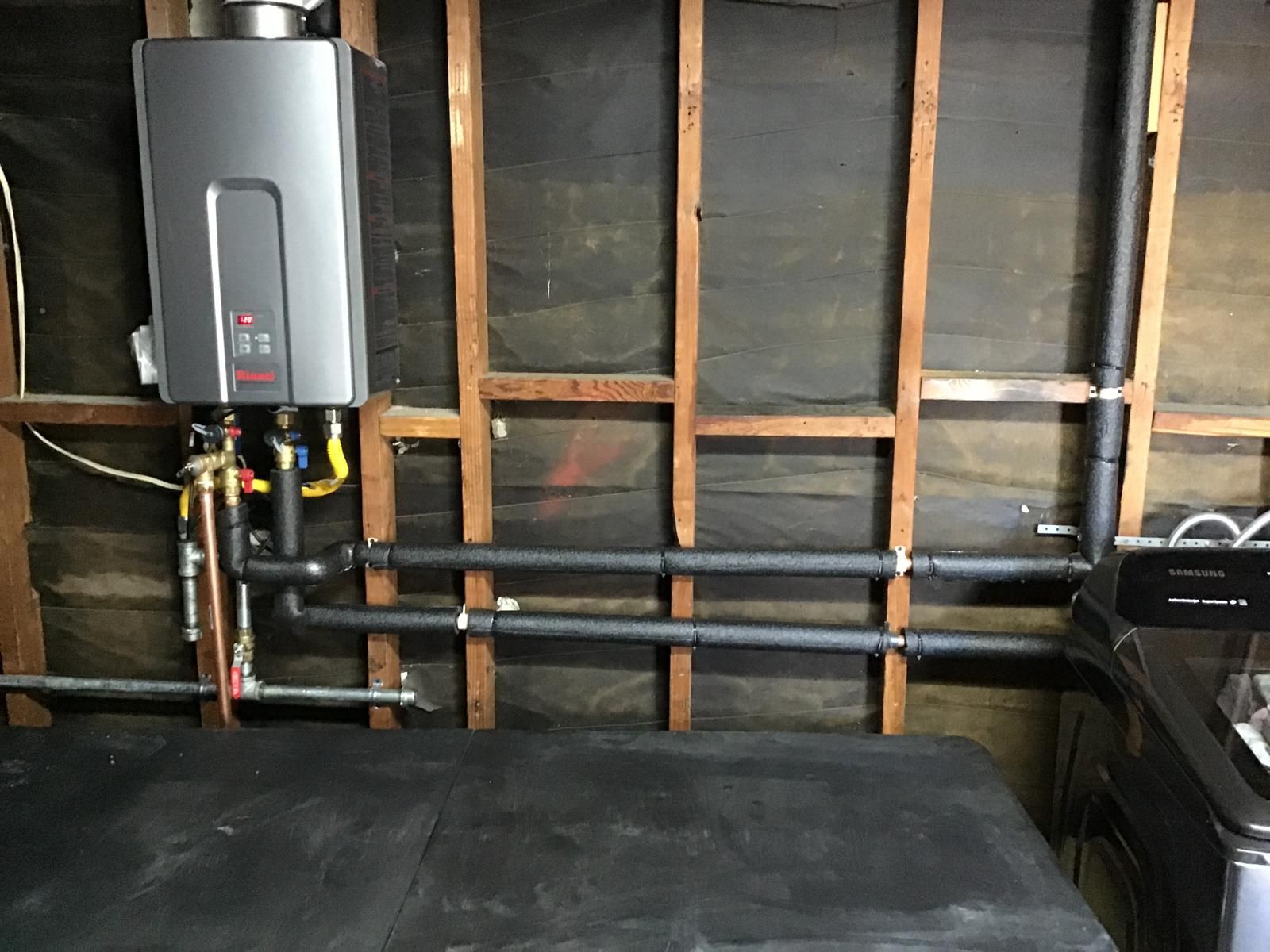 Wall-mounted tankless water heater with insulated plumbing pipes and gas line connections in an unfinished utility room.