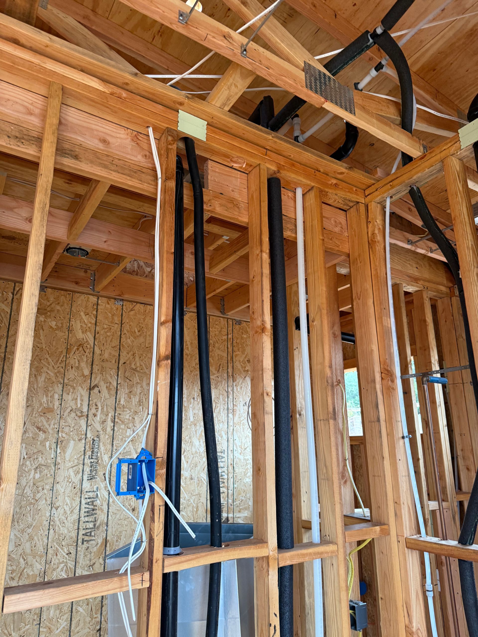 Construction framing with vertical wooden studs, electrical wiring, and black insulated piping inside an unfinished room.