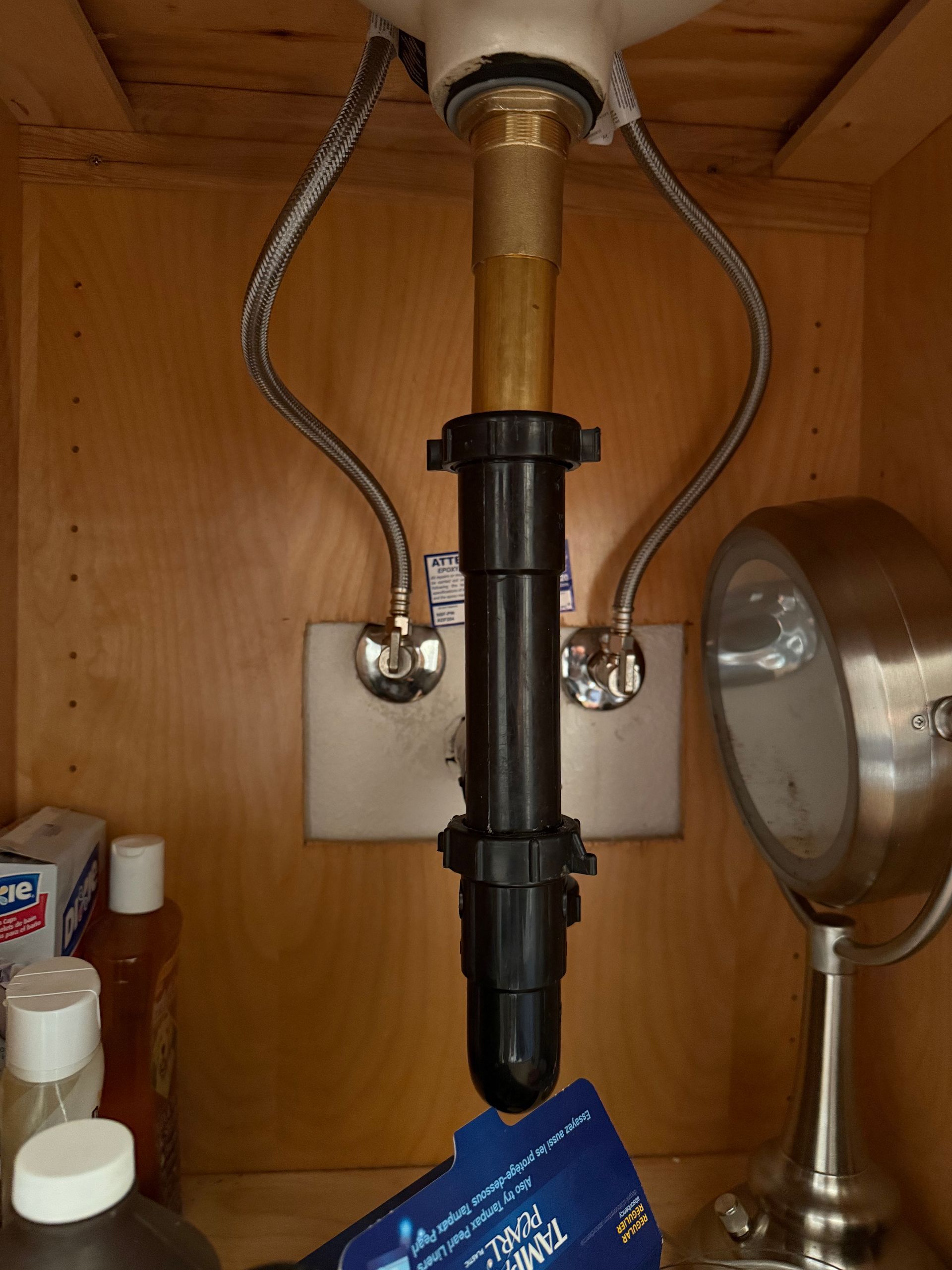 A view inside a bathroom cabinet showing the sink drain plumbing and water supply lines connected to the wall.