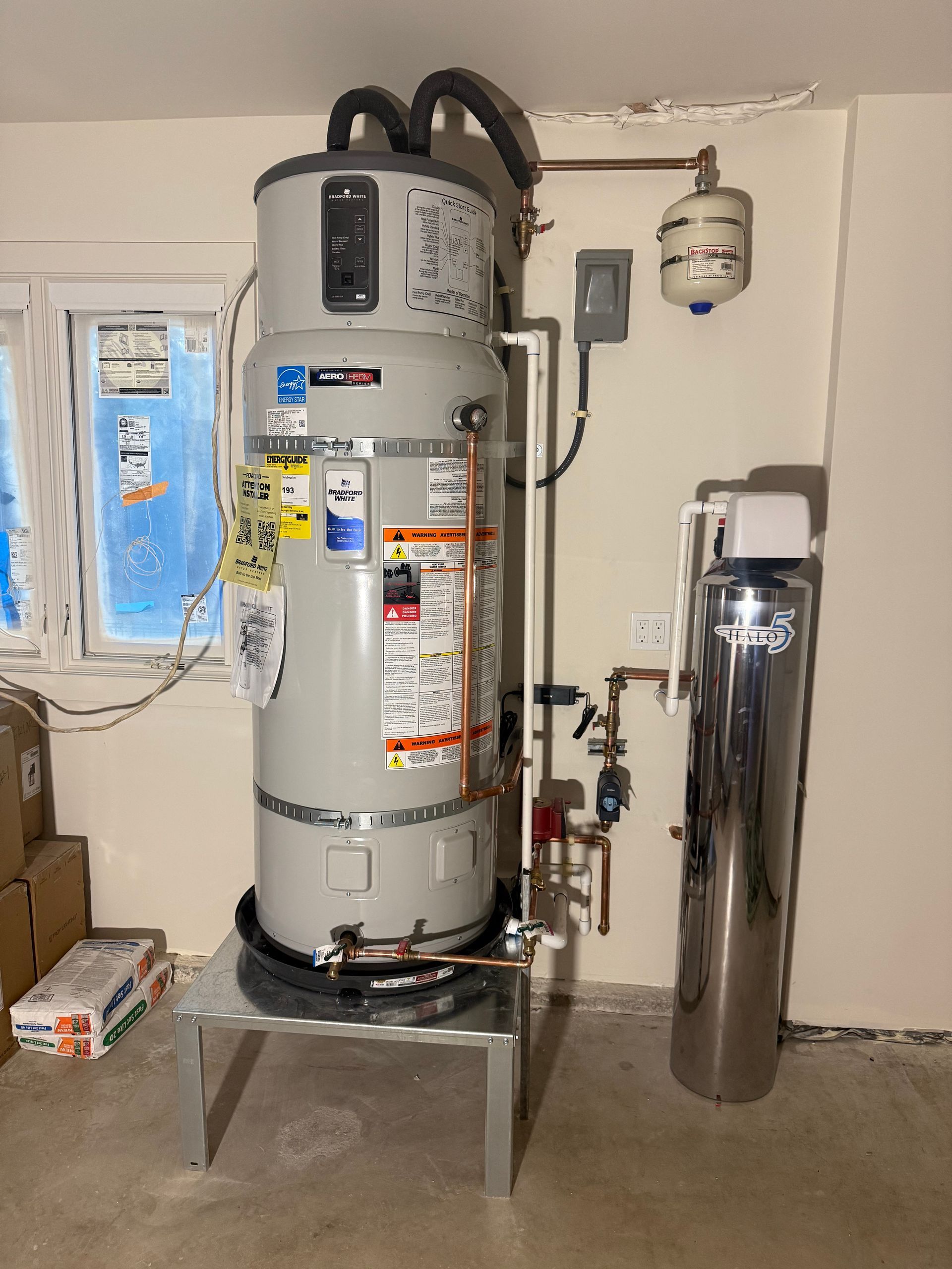 A tall gray electric water heater on a metal stand next to a stainless steel water filtration system in a utility room.