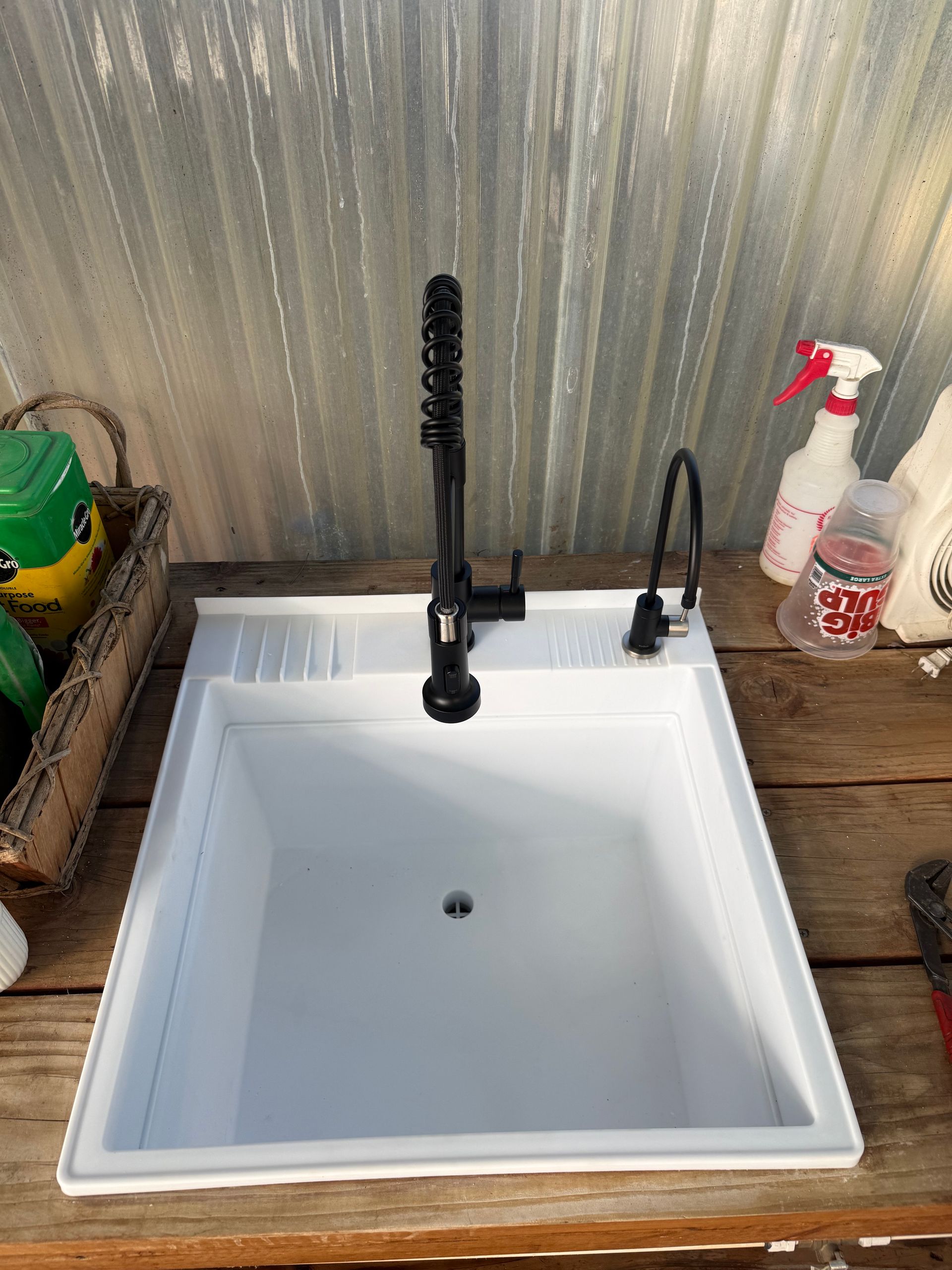 A white kitchen sink with a black industrial-style faucet and small side sprayer, set into a wooden counter.