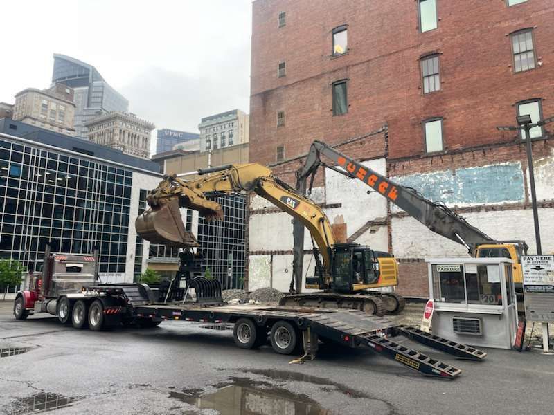 excavator unloading an attachment from the trailer with its claw bucket