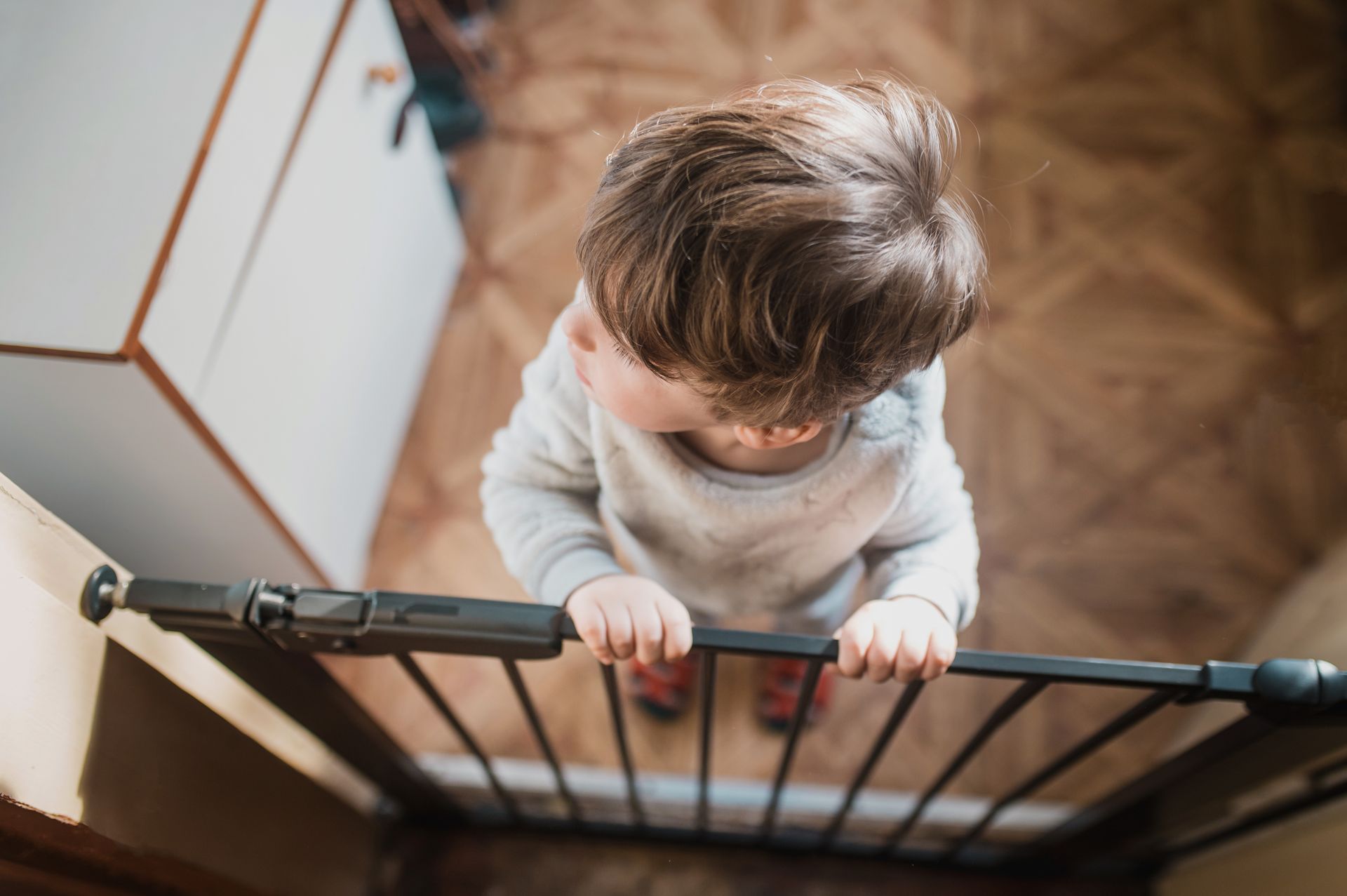 Front view of a curious little boy standing on the opposite side of a child safety gate.